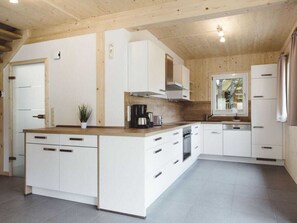 A modern kitchen with white cabinetry, a central island, and a built-in oven. - One-bedroom Cabin (Sankt Georgen am Kreischberg)