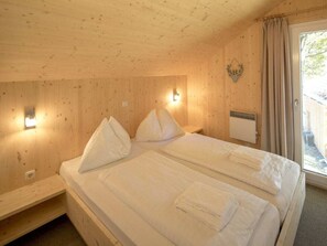 Ein Schlafzimmer einer Holzhütte mit zwei Betten, einem Wandheizgerät und einem Fenster mit Vorhängen.