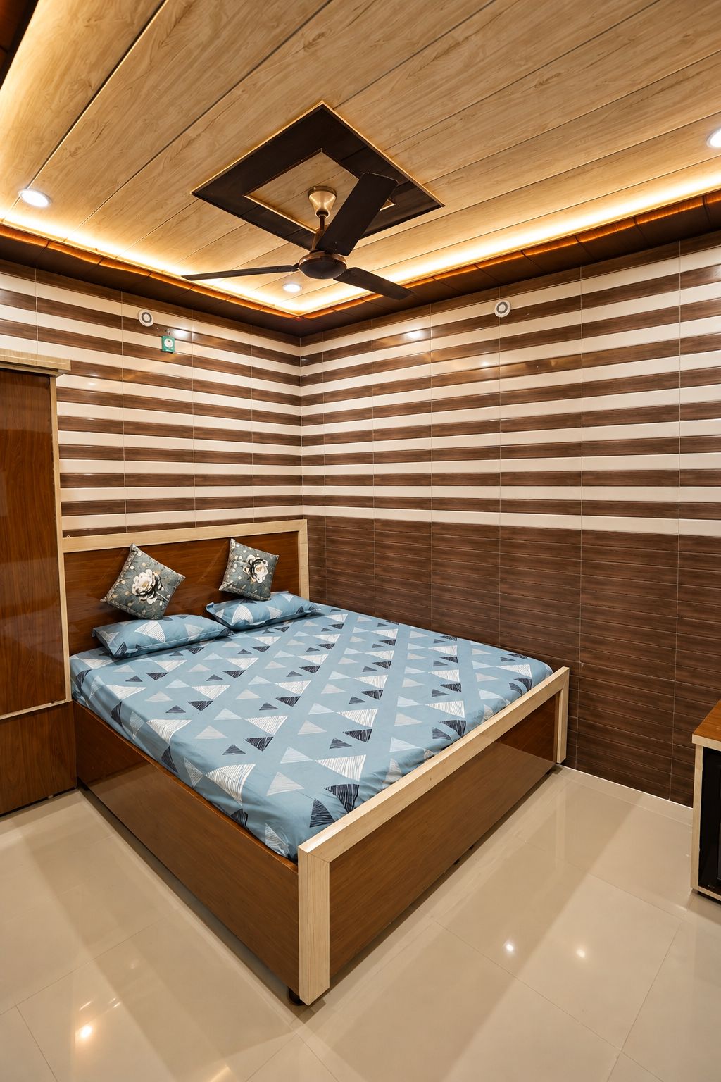 Un dormitorio moderno con una cama de madera, baldosas en la pared a rayas y un ventilador de techo.