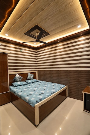 Un dormitorio moderno con techo de madera, cama con colcha de diseño geométrico y ventilador de techo.