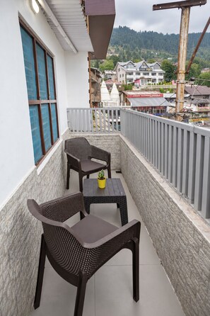 Varanda com duas cadeiras de vime e uma pequena mesa, com vista para uma cidade, edifícios e uma colina ao fundo.