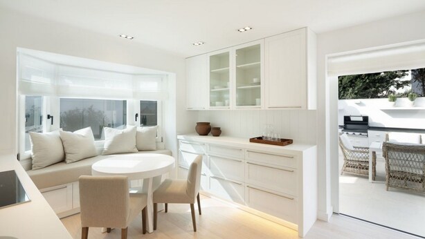 A modern kitchen with white cabinetry, a dining area with a round table and chairs, and a large window providing natural light. - Vrbo Property (Marbella)