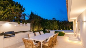 An outdoor patio with a dining table and chairs, a grill, and a white wall with potted plants. - Vrbo Property (Marbella)