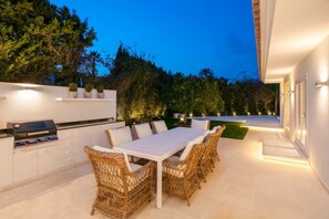 Eine Außenpatio mit Esstisch und Stühlen, einem Grill und einer weißen Mauer mit Blumentöpfen.