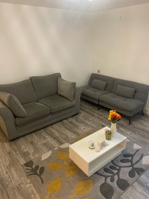 Ein Wohnzimmer mit zwei grauen Sofas, einem weißen Couchtisch mit Dekoration und einem gemusterten Teppich.
