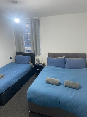Ein Hotelzimmer mit zwei Betten, einem Nachttisch, einer Lampe und einem Fenster mit Vorhängen.