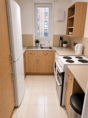 A compact kitchen with a refrigerator, stove, sink, and wooden cabinets. - Centrally located Flat in the Heart of Kennington (KENNINGTON)