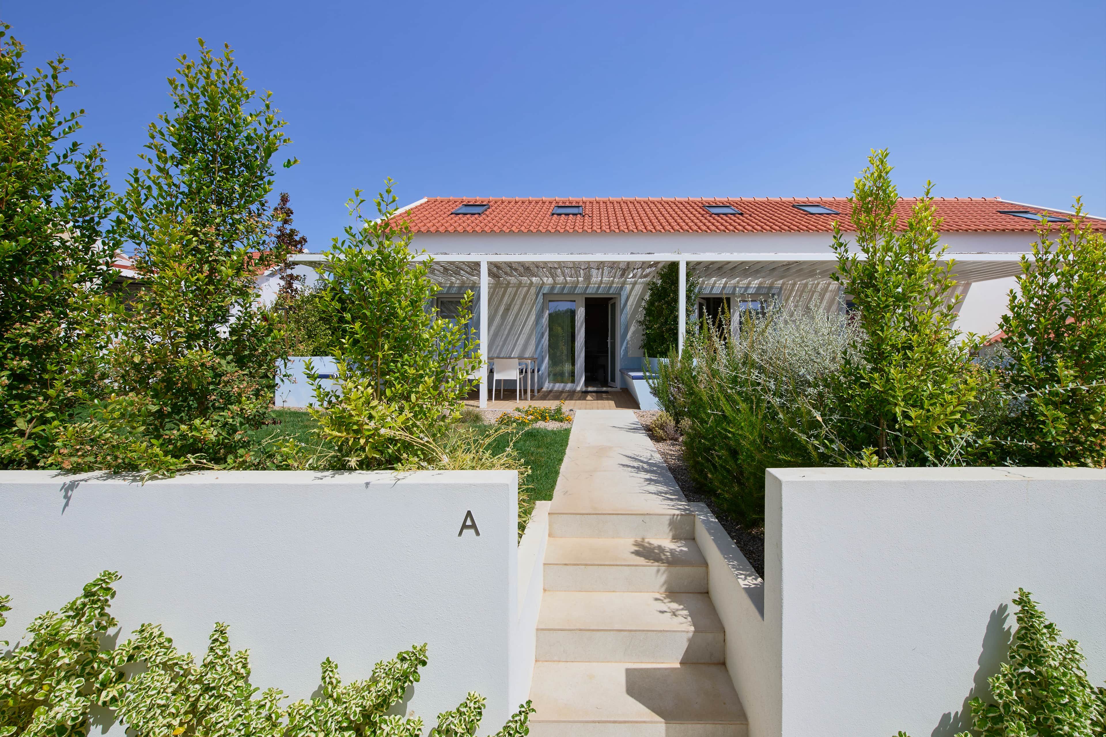 A modern house with a red-tiled roof, a covered porch, and a pathway leading to the entrance.