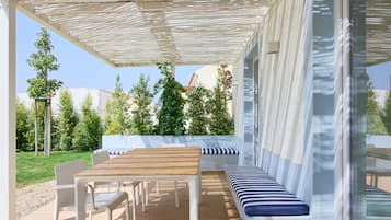 An outdoor patio with a wooden table and chairs, a bench with striped cushions, and a pergola providing shade.