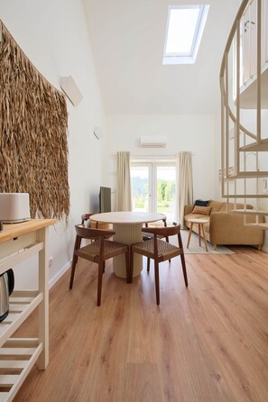 Ein modernes Wohnzimmer mit einem runden Holztisch, zwei Stühlen, einer Couch und einem großen Fenster mit Vorhängen.