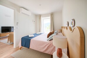 Ein Hotelzimmer mit Bett, Schreibtisch mit Fernseher, Klimaanlage und einem Fenster mit Vorhängen.