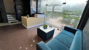 Ein Hotel-Empfangsbereich mit einer Rezeption, einem blauen Sofa, einem Couchtisch und Blick durch eine Glastrennwand.