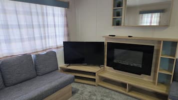 A living room with a grey sofa, a flat-screen TV on a wooden stand, a fireplace, and a window with curtains.