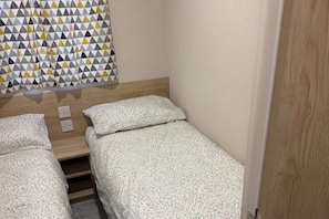 A small, compact room with two single beds, a wooden headboard, and a patterned wall decoration. - 3 Bed Caravan - Free Parking & Wifi (Fleetwood)