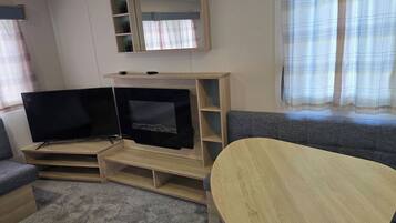 A living room with a flat-screen TV on a wooden stand, a grey sofa, and a small table.