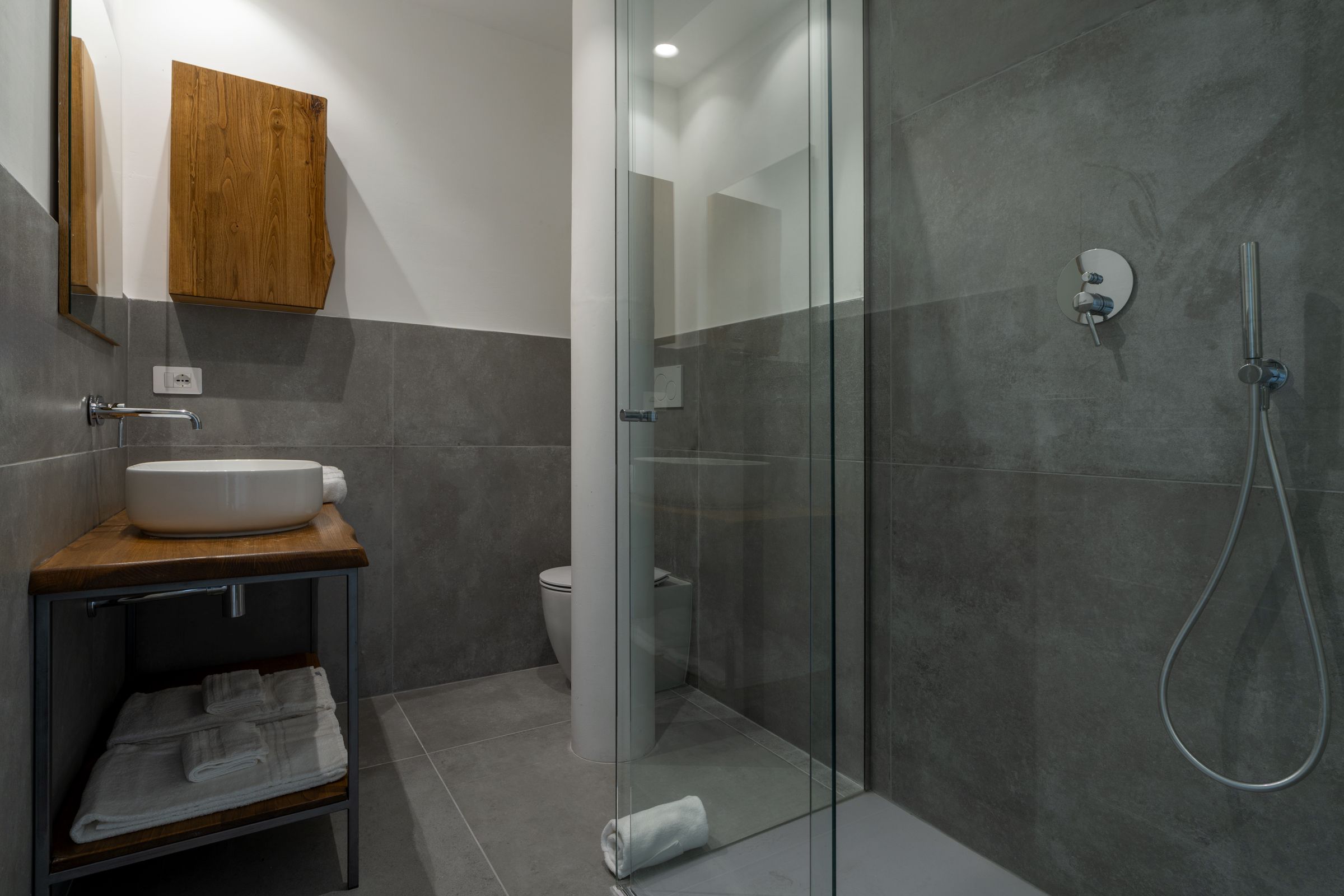 Un bagno moderno con cabina doccia in vetro, un mobile vanitario in legno e un lavandino bianco.