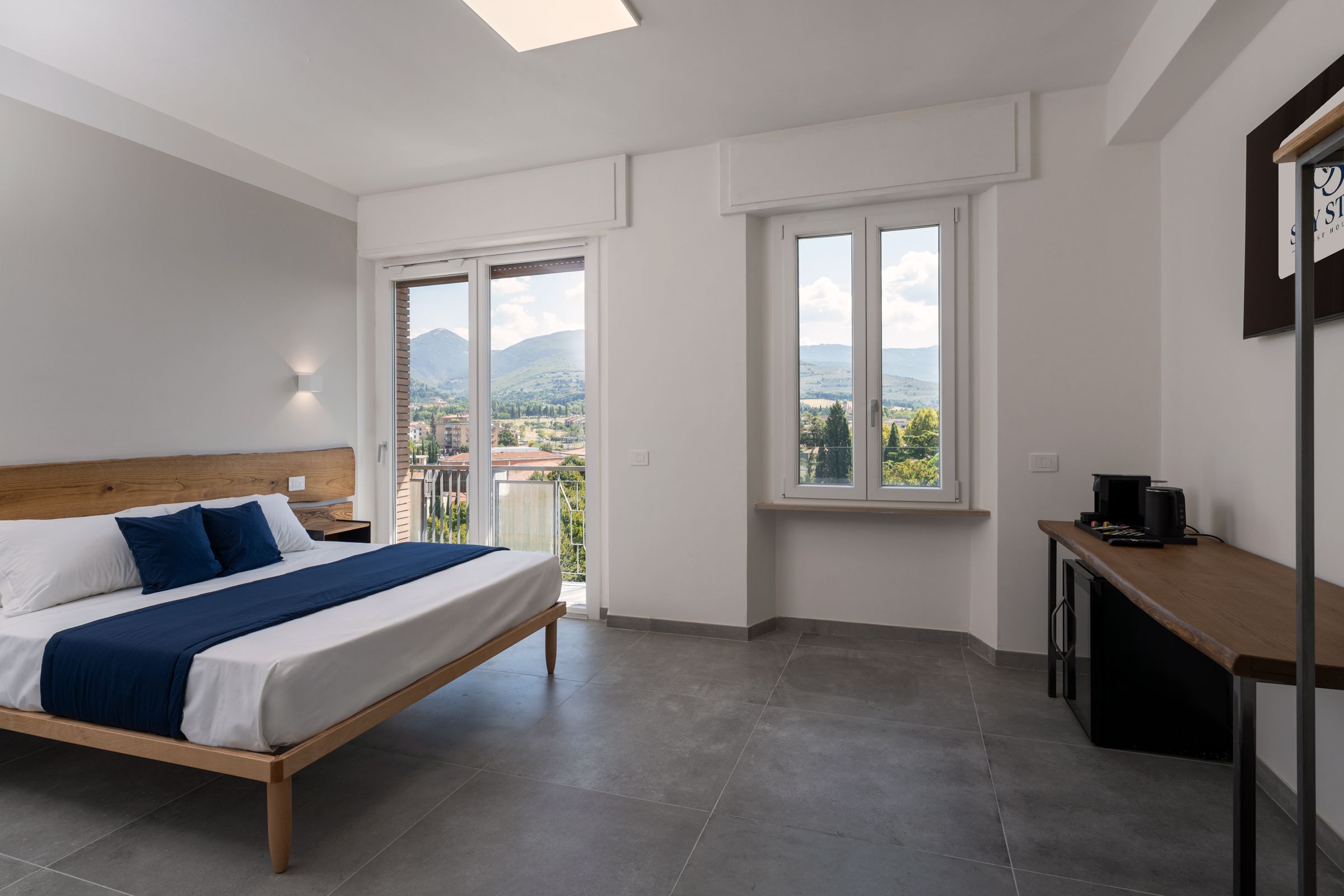 Ein Schlafzimmer mit Bett, Schreibtisch und Blick auf Stadt und Berge.