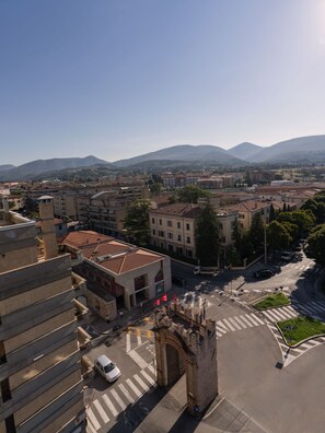 A cityscape with a prominent building featuring a large archway, a crosswalk, and a clear view of the surrounding urban area and distant mountains. - Sky Star Luxury Guest House Luna Queen Deluxe (Foligno)