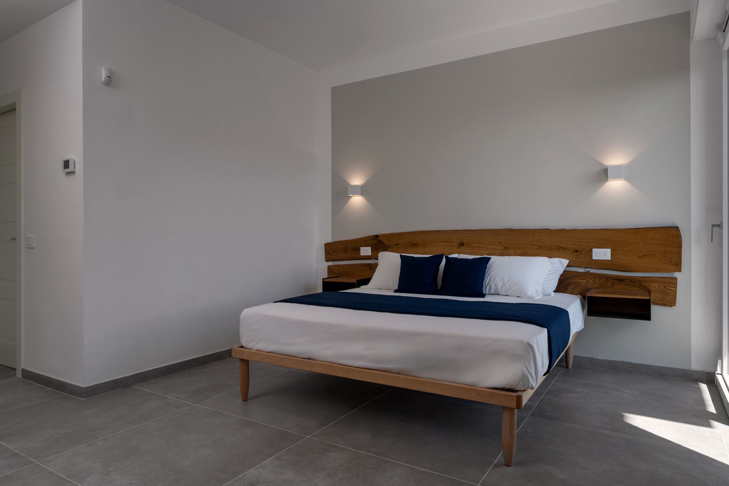 Una camera da letto moderna con una struttura letto in legno, biancheria da letto bianca e due luci a parete.