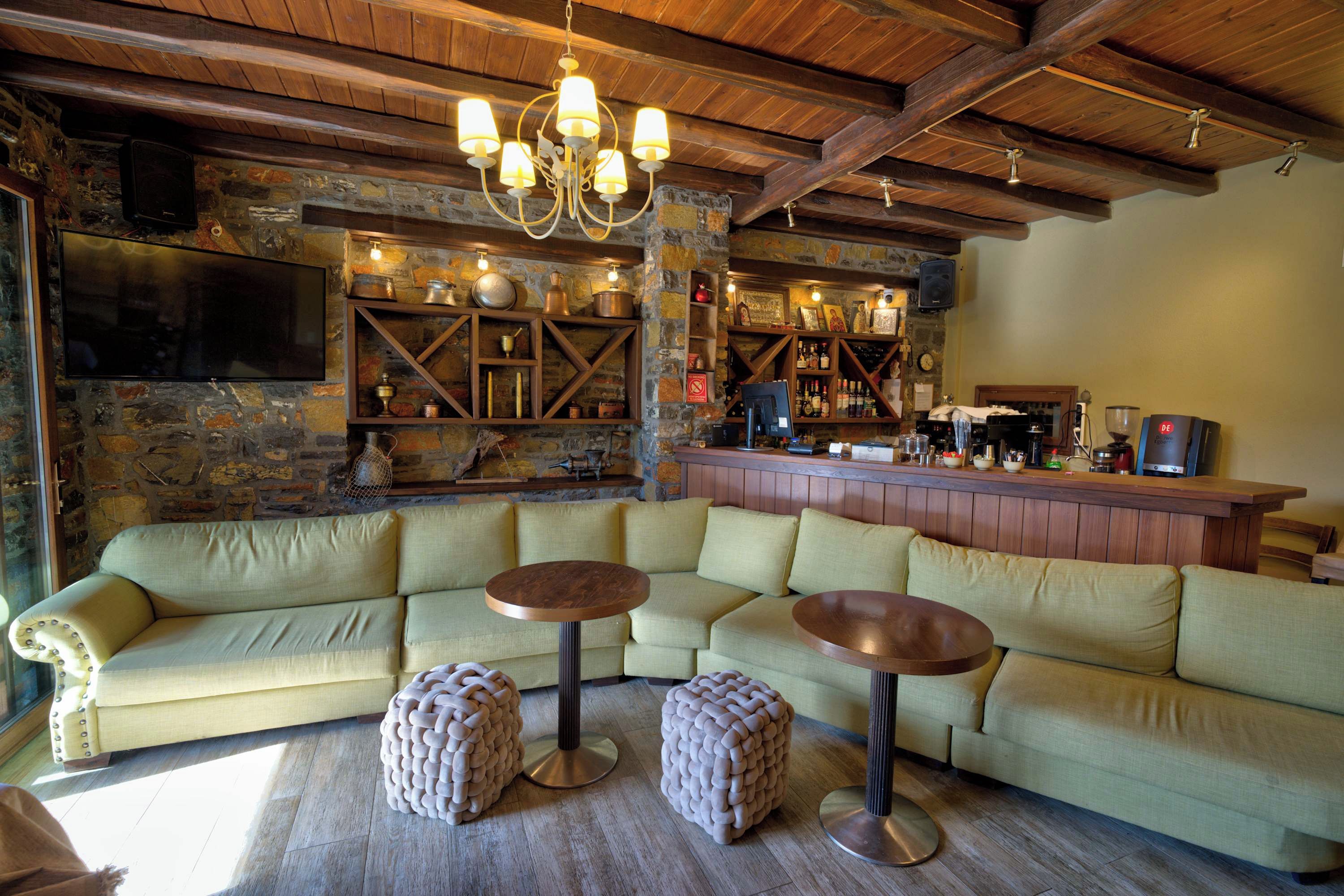 Eine gemütliche Bar mit einer Steinwand, Holzbalkendecke und einem großen Ecksofa mit Hockern.