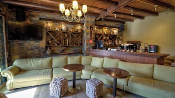 Eine gemütliche Bar mit einer Steinwand, Holzbalkendecke und einem großen Ecksofa mit Hockern.