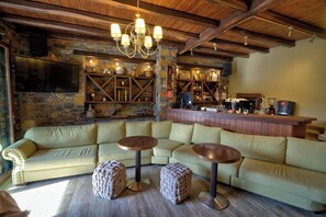 Angolo bar accogliente con parete in pietra, soffitto in legno e un ampio divano componibile con poggiapiedi.