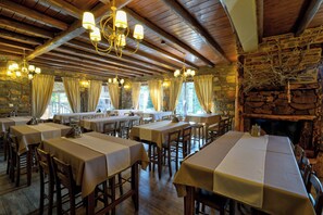 Un ristorante con diversi tavoli, travi in legno, pareti in pietra e un camino.