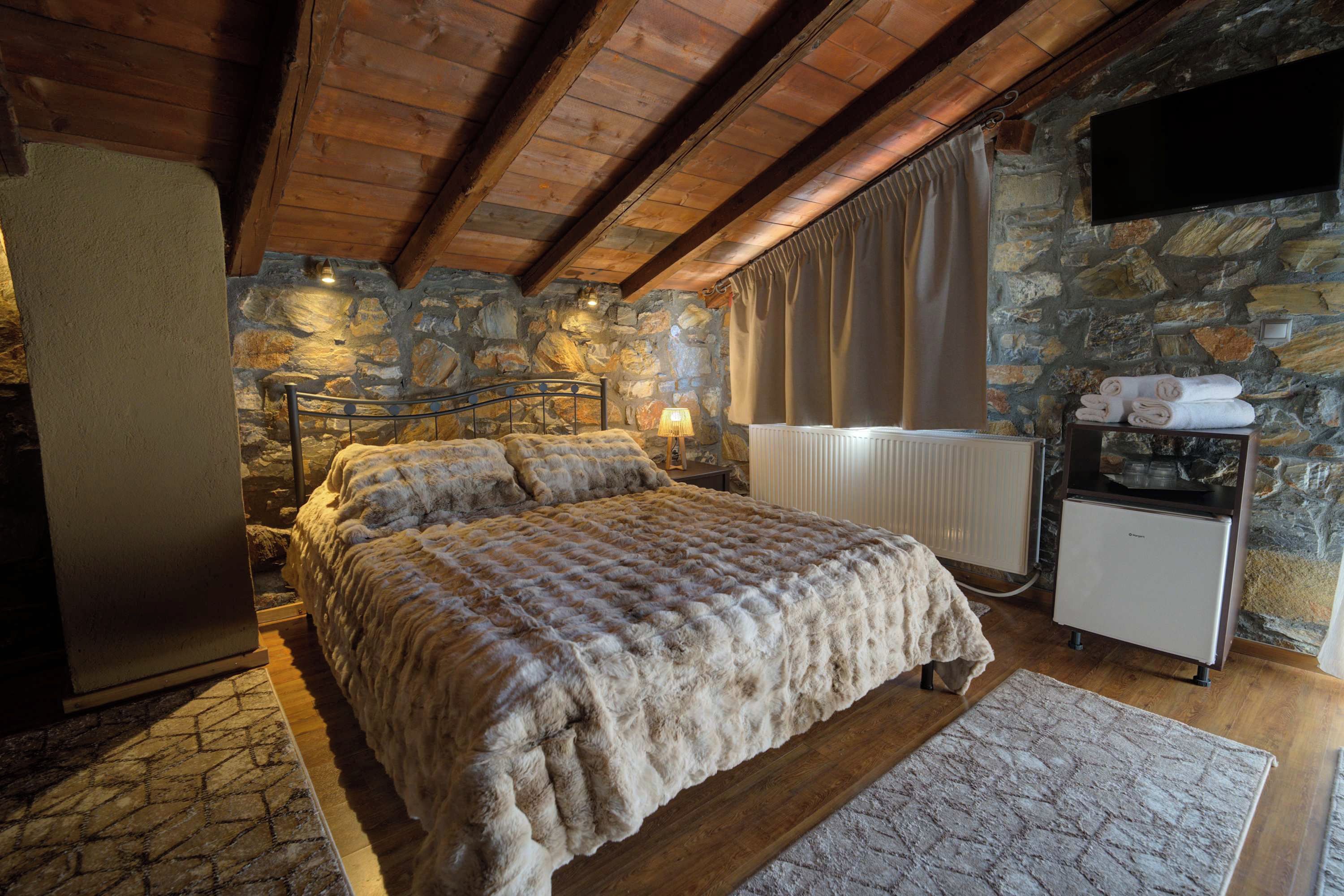 Ein Schlafzimmer mit einer Steinwand, einem Bett mit einer flauschigen Decke, einem Heizkörper und einem kleinen Kühlschrank.