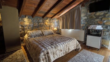 Ein Schlafzimmer mit einer Steinwand, einem Bett mit einer flauschigen Decke, einem Heizkörper und einem kleinen Kühlschrank.