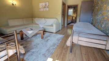A cozy living room with a sofa, a small table, a bed, and a stone wall.