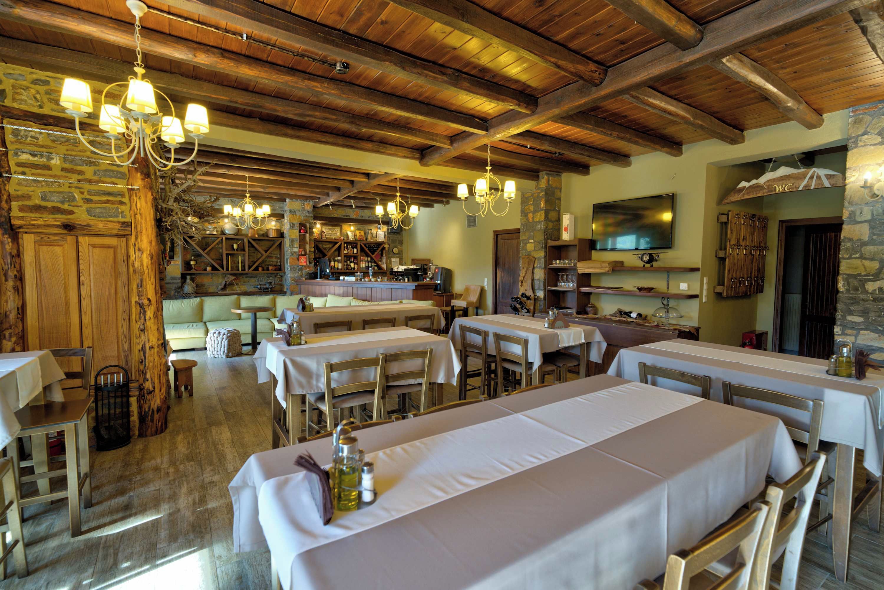 Ein rustikales Restaurant mit Holzbalken, Steinwänden und mehreren Esstischen.