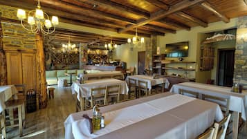Ein rustikales Restaurant mit Holzbalken, Steinwänden und mehreren Esstischen.