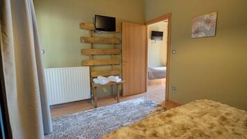 Quarto com parede de ripas de madeira, televisão montada, porta de madeira, radiador, um banco com toalhas, tapete e um tapete fofo no chão.