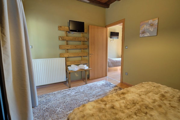 A room with a wooden slat wall, a television mounted on it, a wooden door, a radiator, a bench with towels, a rug, and a fluffy rug on the floor.