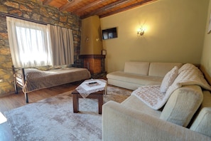 A cozy living room with a stone wall, a fireplace, a sofa, a bed, and a television.