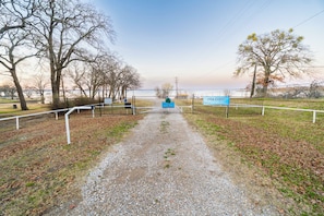 A gravel path leading to a gate with a blue sign, surrounded by leaf-covered ground and trees. - Quiet 3-bedroom house in charming West Tawakoni beside the lake (Quinlan)