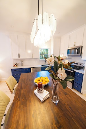 A modern kitchen with white cabinets, a wooden dining table, and a decorative white feather chandelier. - Quiet 3-bedroom house in charming West Tawakoni beside the lake (Quinlan)