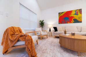 A living room with a white sofa, a wooden coffee table, and a colorful abstract painting on the wall. - Quiet 3-bedroom house in charming West Tawakoni beside the lake (Quinlan)