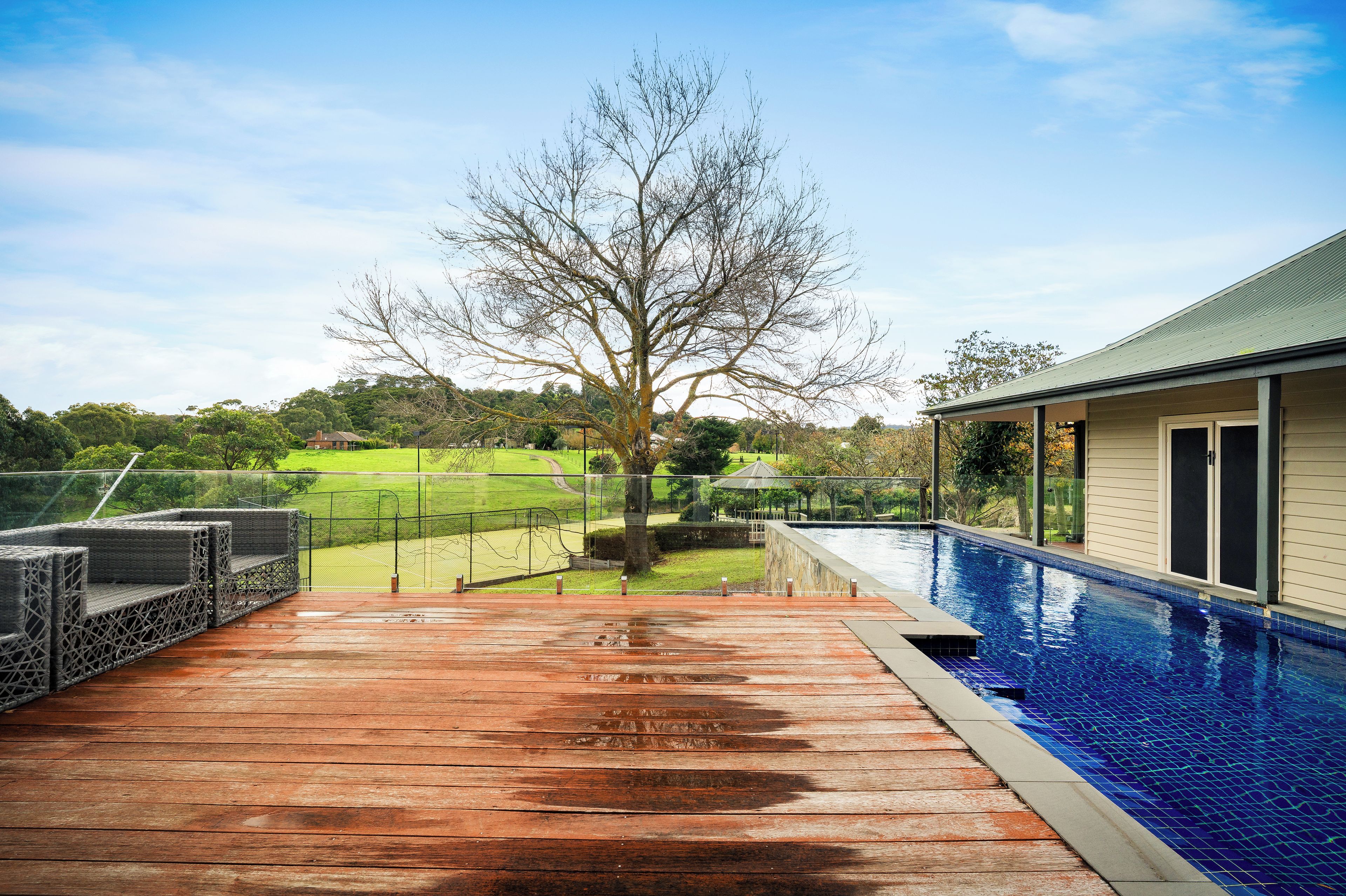 A swimming pool with a wooden deck and a view of a park.