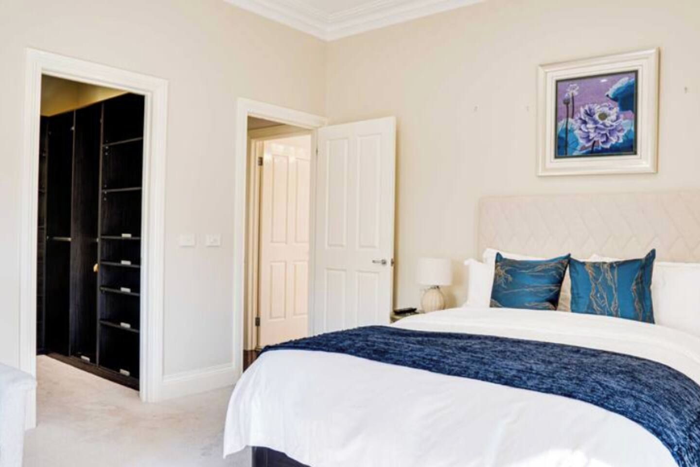 A bedroom with a bed, a nightstand, a lamp, a painting, and a closet.