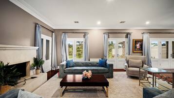 A living room with a grey sofa, a coffee table, a fireplace, and a view through the windows.