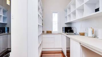 A narrow kitchen with white cabinetry, a wooden floor, and a window providing natural light.