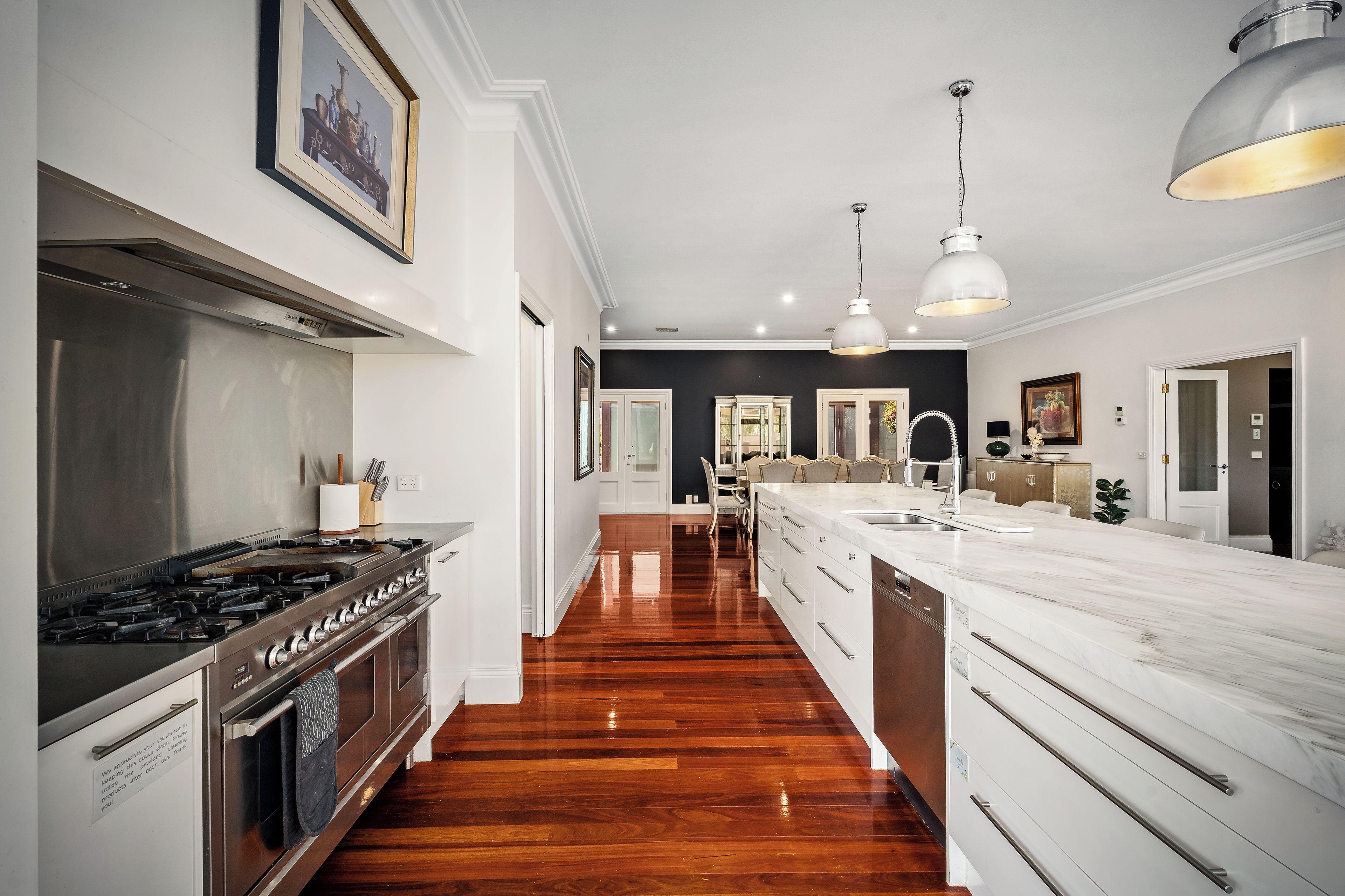 A modern kitchen with a stainless steel range, a wooden floor, and a large island with a sink.