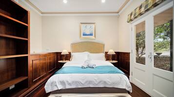 A hotel room with a bed, two bedside tables, a painting on the wall, and a view through a door.