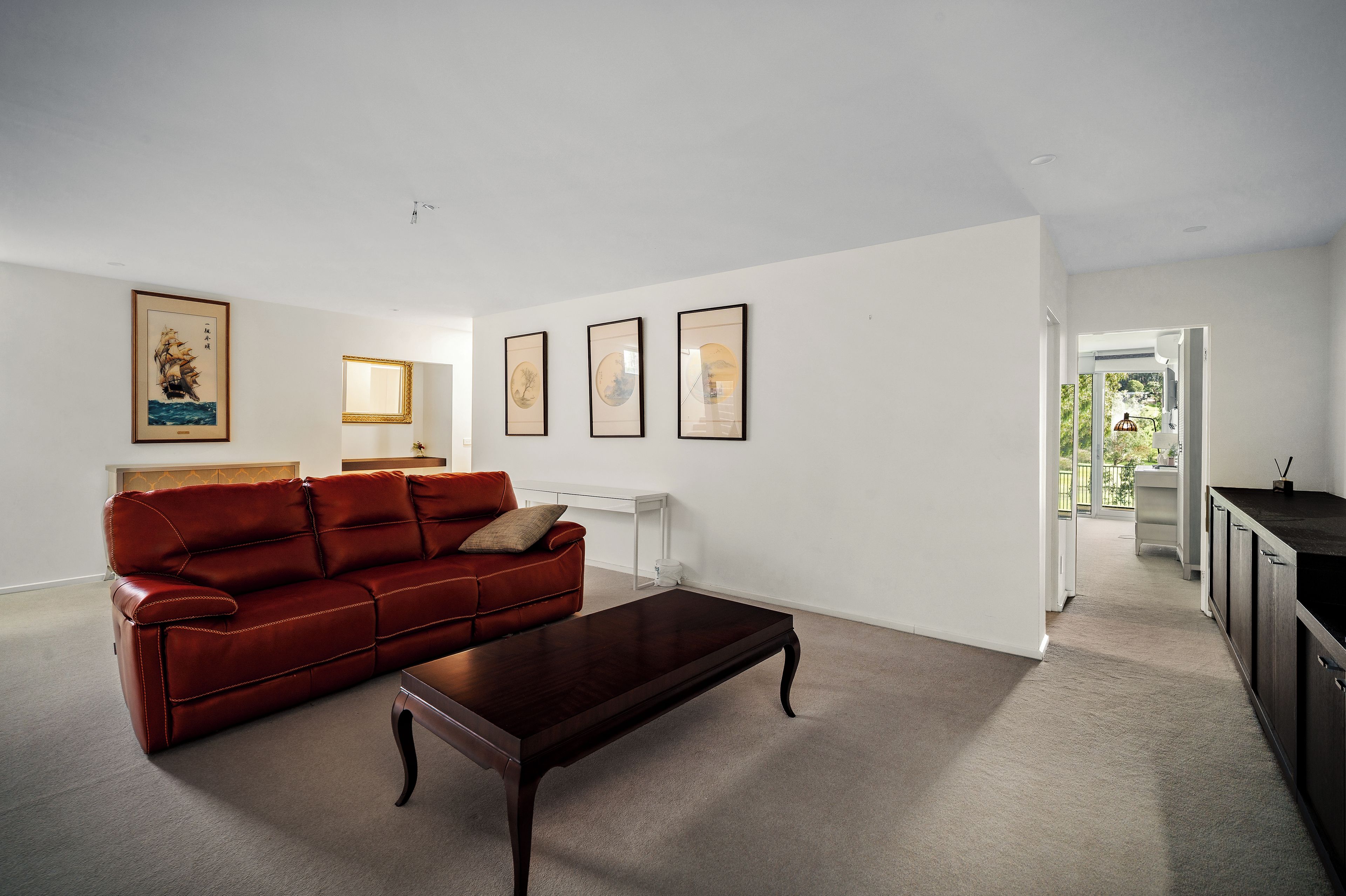 A living room with a red leather sofa, a dark wooden coffee table, and three framed artworks on the wall.