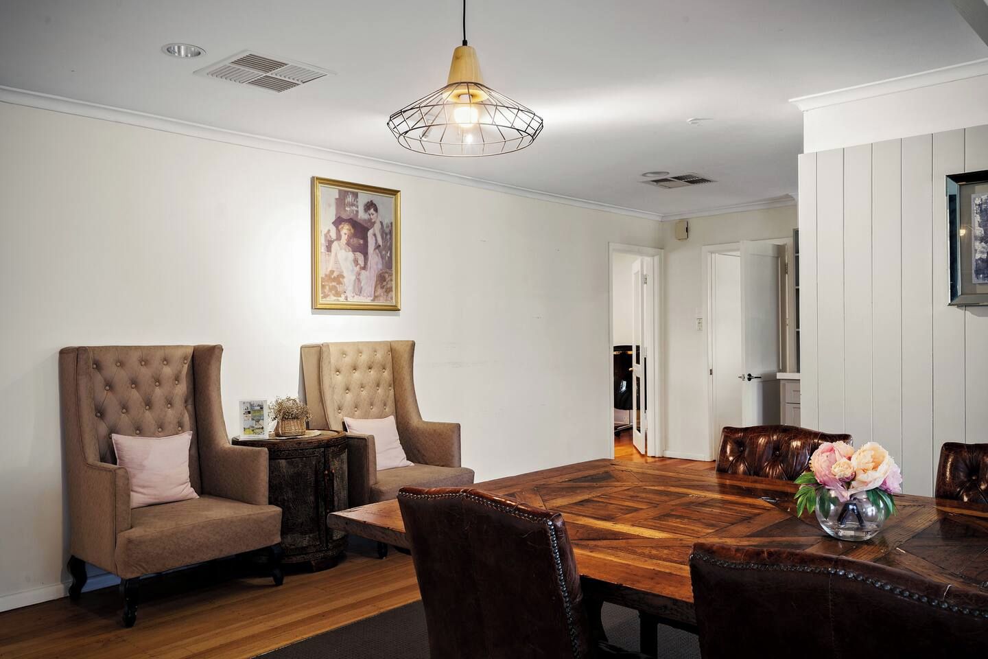 A dining room with a wooden table, leather chairs, a tufted armchair, a side table, and a pendant light.