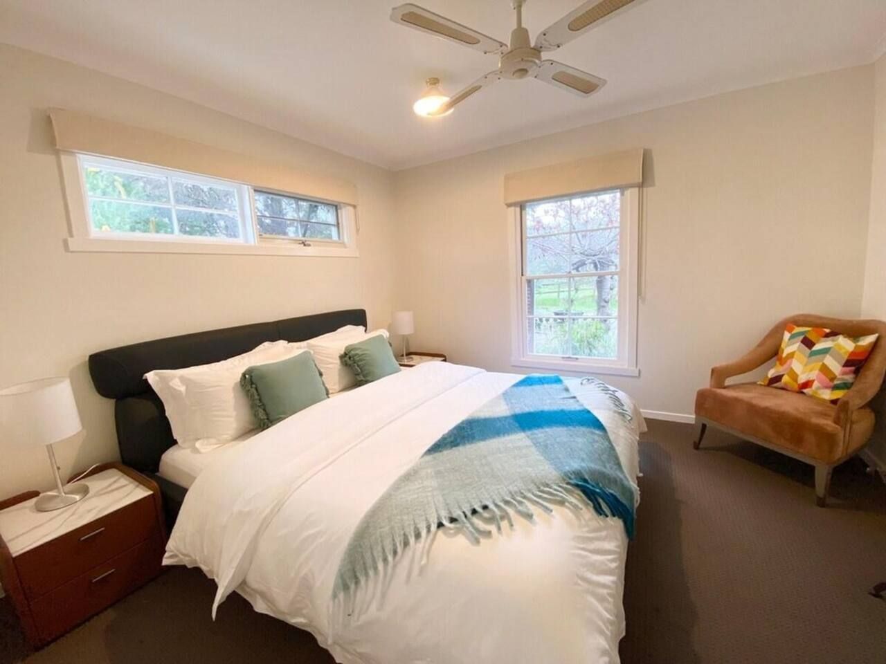 A bedroom with a bed, nightstands, a chair, and windows.