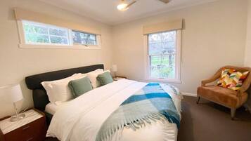 A bedroom with a bed, nightstands, a chair, and windows.