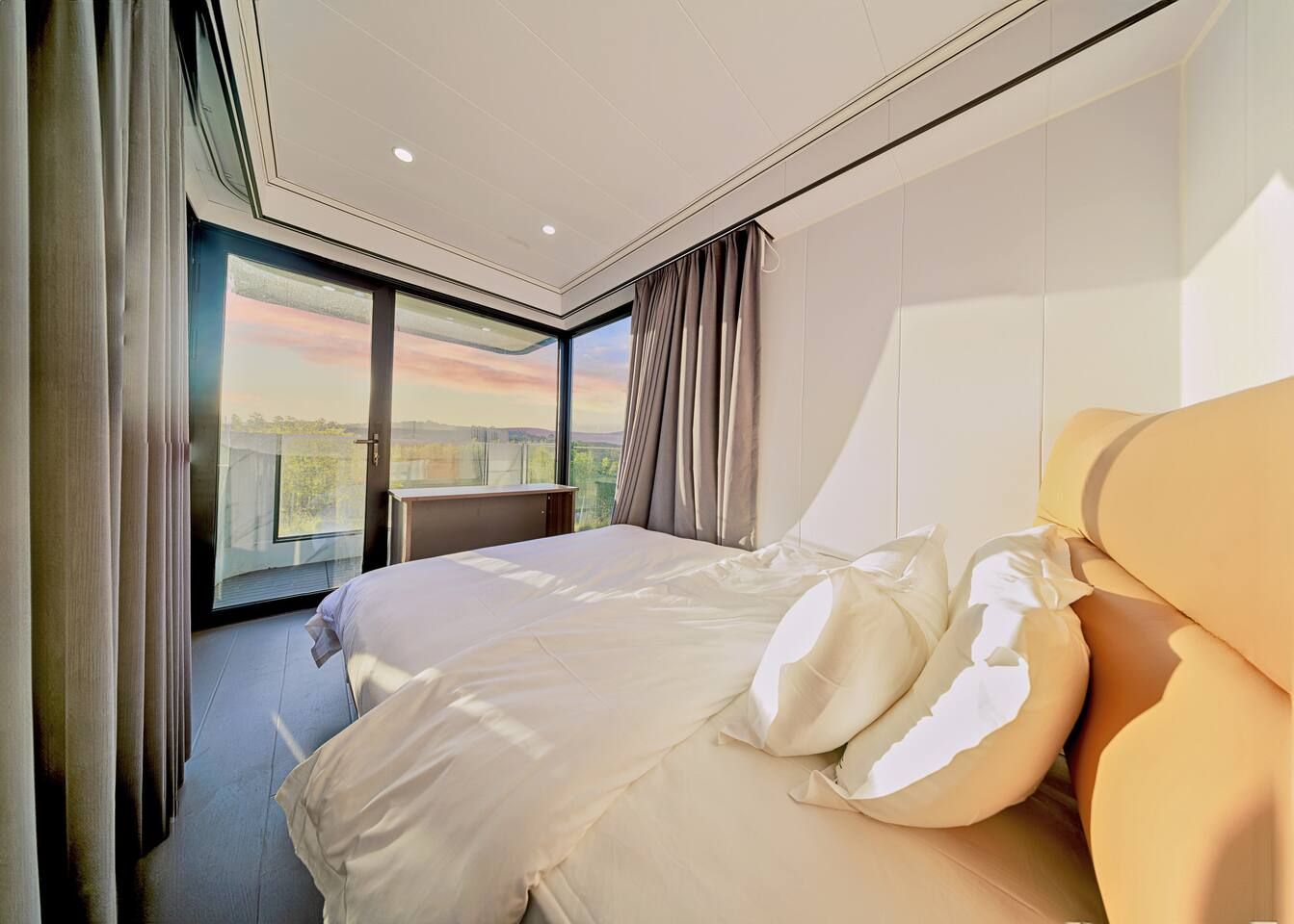 A modern bedroom with a large bed, a view of the outdoors, and a large window.