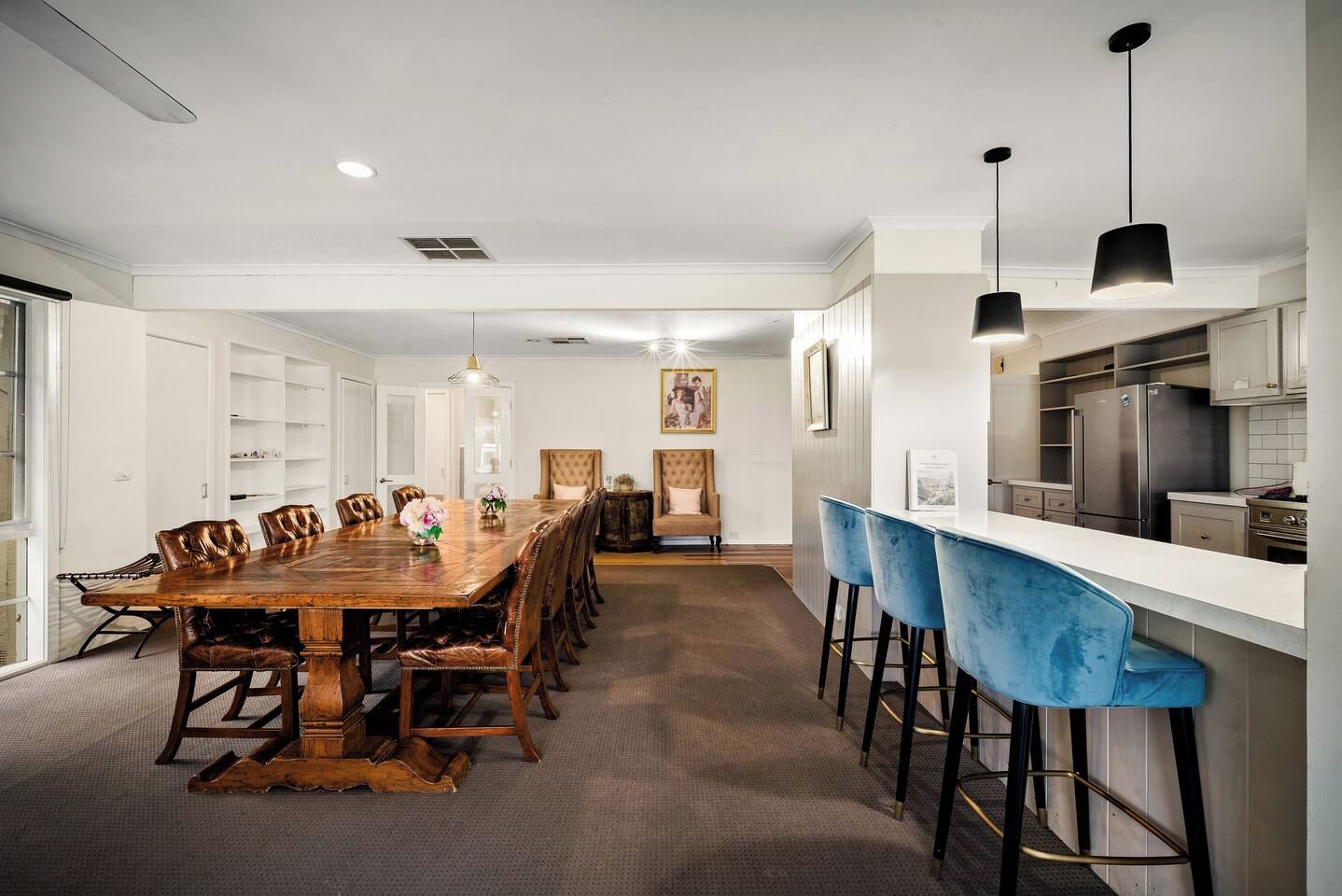 A modern dining area with a long wooden table, leather chairs, and a bar with blue barstools.